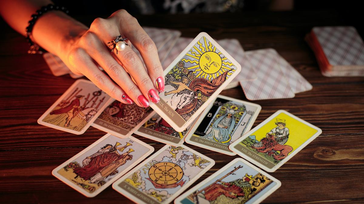 A hand lifting The Sun card from a spread of Major Arcana cards on a wooden table.