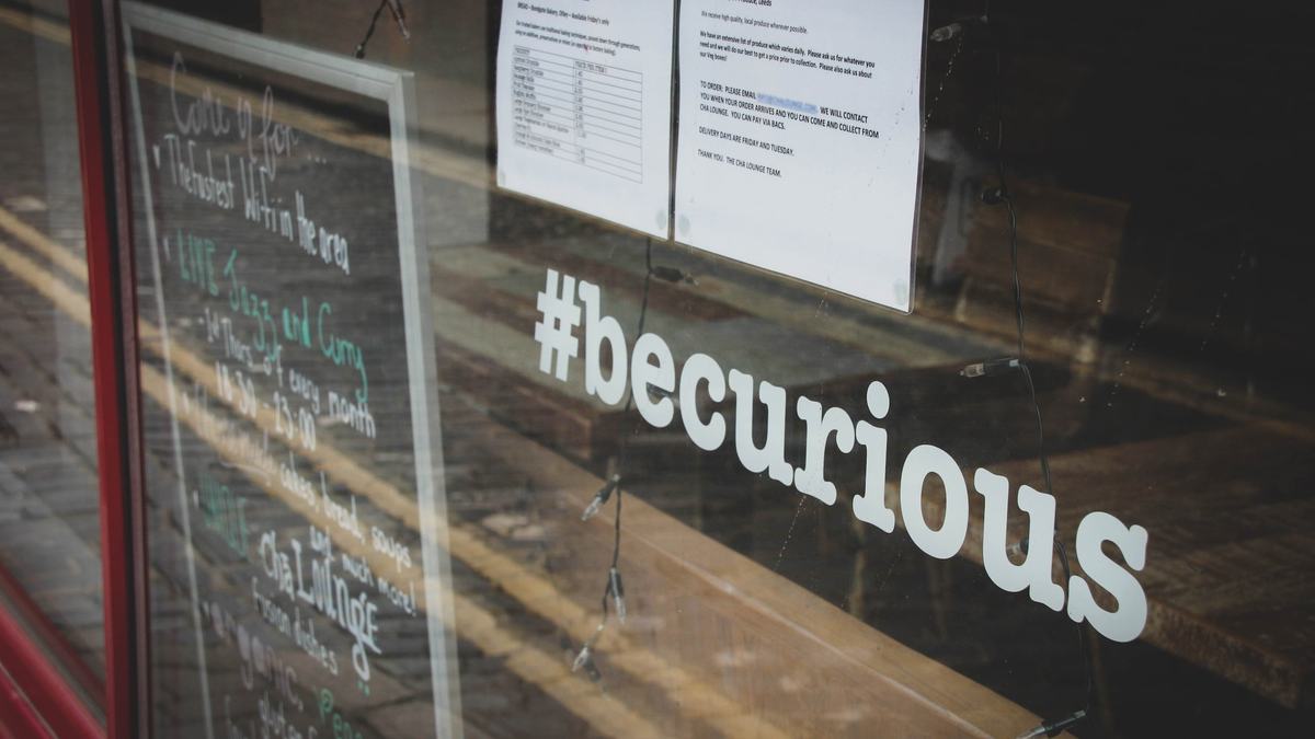 A café window with “#becurious” lettered across the glass.